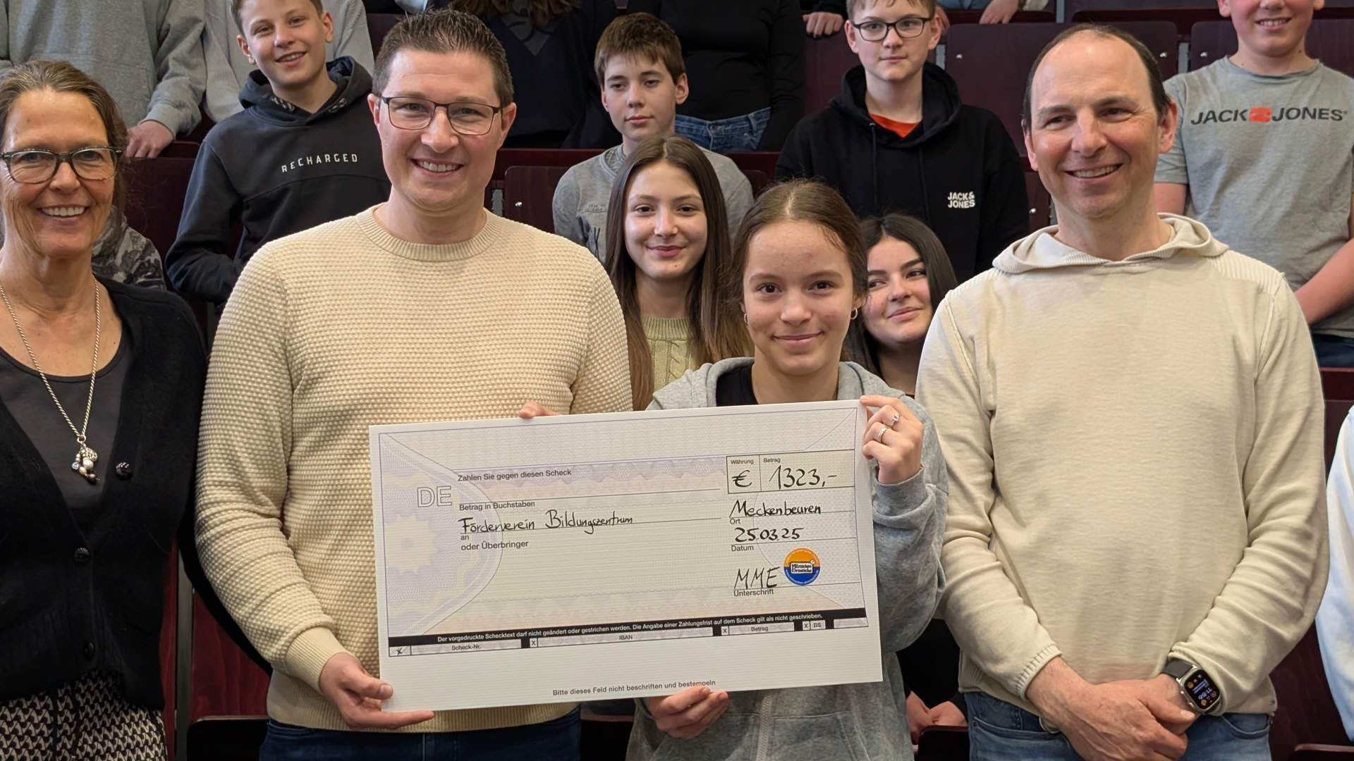 Frau Wiedmann, Rektorin des BZM, Herr Walker CO-Rektor des BZM, ein Elternrat und die Schüler im Hintergrund lächeln mit einem Scheck des Fördervereins in die Kamera.