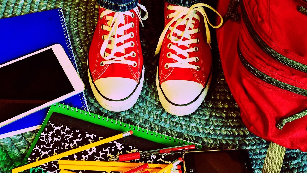 Rote Schuhe, ein Rucksack, ein Handy sowie wie ein Block und Stifte