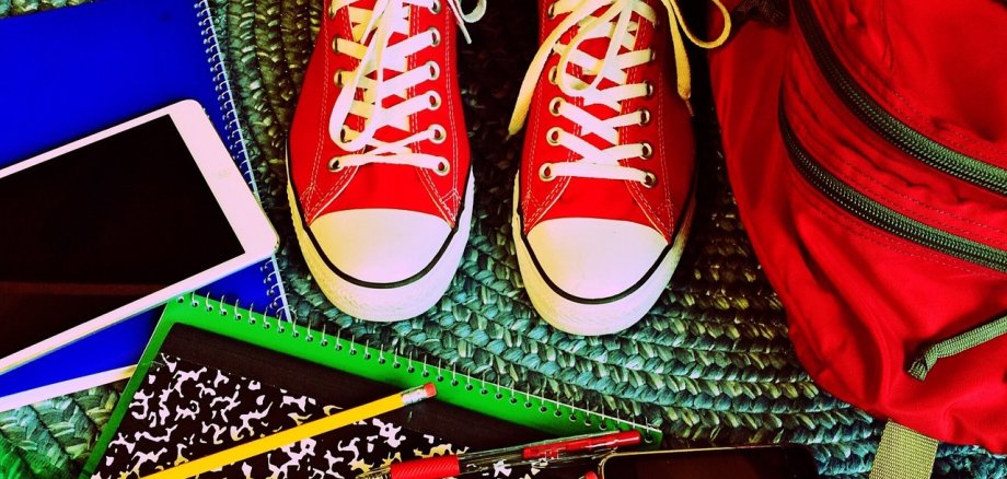 Rote Schuhe, ein Rucksack, ein Handy sowie wie ein Block und Stifte 