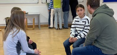 Nils Keading spricht mit den Gemeindedetektiven. Die Kinder hören ihm gespannt zu. Im Hintergrund zeigt Bürgermeister Georg Schellinger den Gemeindedetektiven Orte auf der Karte Meckenbeurens