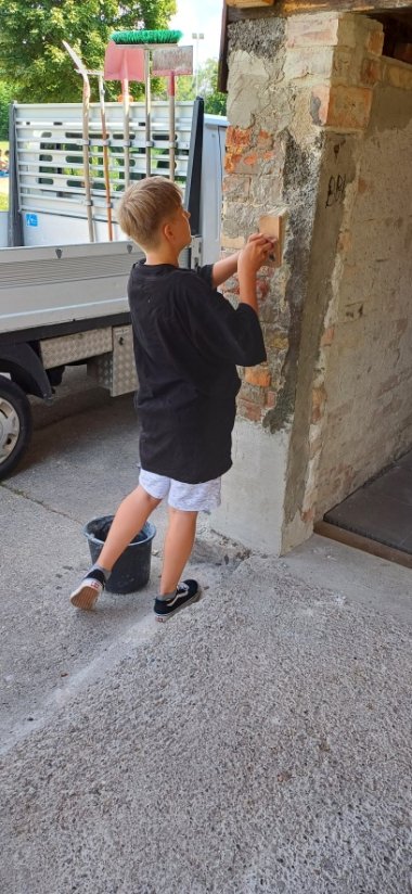 EIn Junger Helfer spachtelt die Wand des Jugendhauses an die Wand
