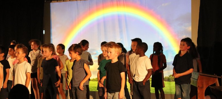 Schülertheater auf einer Bühne mit Regenbogen und vielen Grundschülern