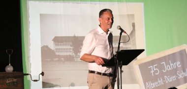 Georg Schellinger spricht vor einer Leinwand auf dem Schuljubiläum