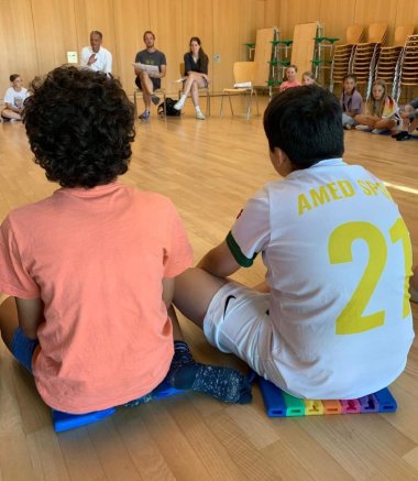 Zwei Schüler sitzen im Kreis und hören aufmerksam zu.