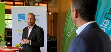 Teilnehmer des symbolischen Startschusses weiße Flecken im Trauzimmer der Gemeinde Meckenbeuren vor Stehtischen und Holzwand