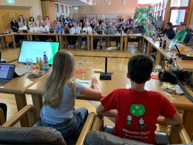Grundschüler zum Teil in roten T Shirts im Großen Sitzungssaal der Gemeinde tragen etwas vor