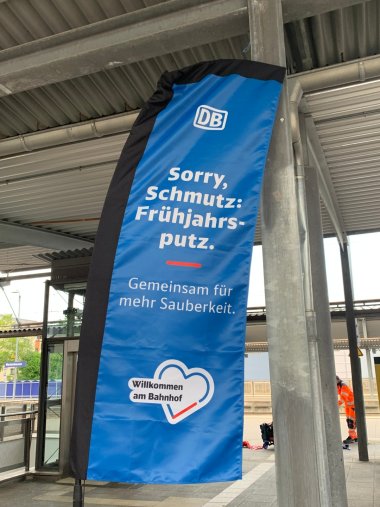 Bahnhofsvorplatz Meckenbeuren mit Blumen und Menschen, die saubermachen