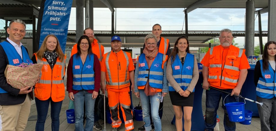 Bahnhofsvorplatz Meckenbeuren mit Blumen und Menschen, die saubermachen
