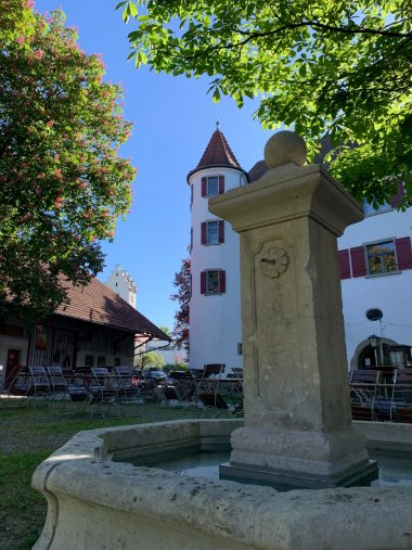 weiße Außenfassade des etwa 500 Jahre alten Schloss Brochezell mit Türmen und Brunnen davor