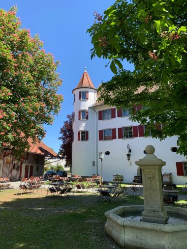 weiße Außenfassade des etwa 500 Jahre alten Schloss Brochezell mit Türmen und Brunnen davor